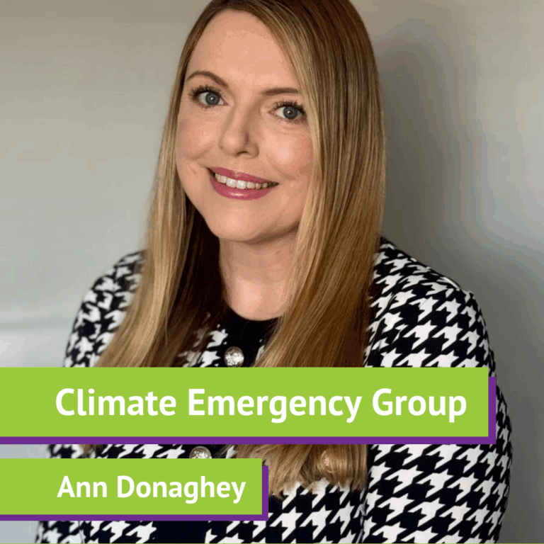 Portrait of a woman with long, light brown hair and fair skin, smiling, wearing a black and white houndstooth patterned blazer with silver buttons, against a plain background. On the image, text reads 'Climate Emergency Group' and 'Ann Donaghey' in white font with a green background.