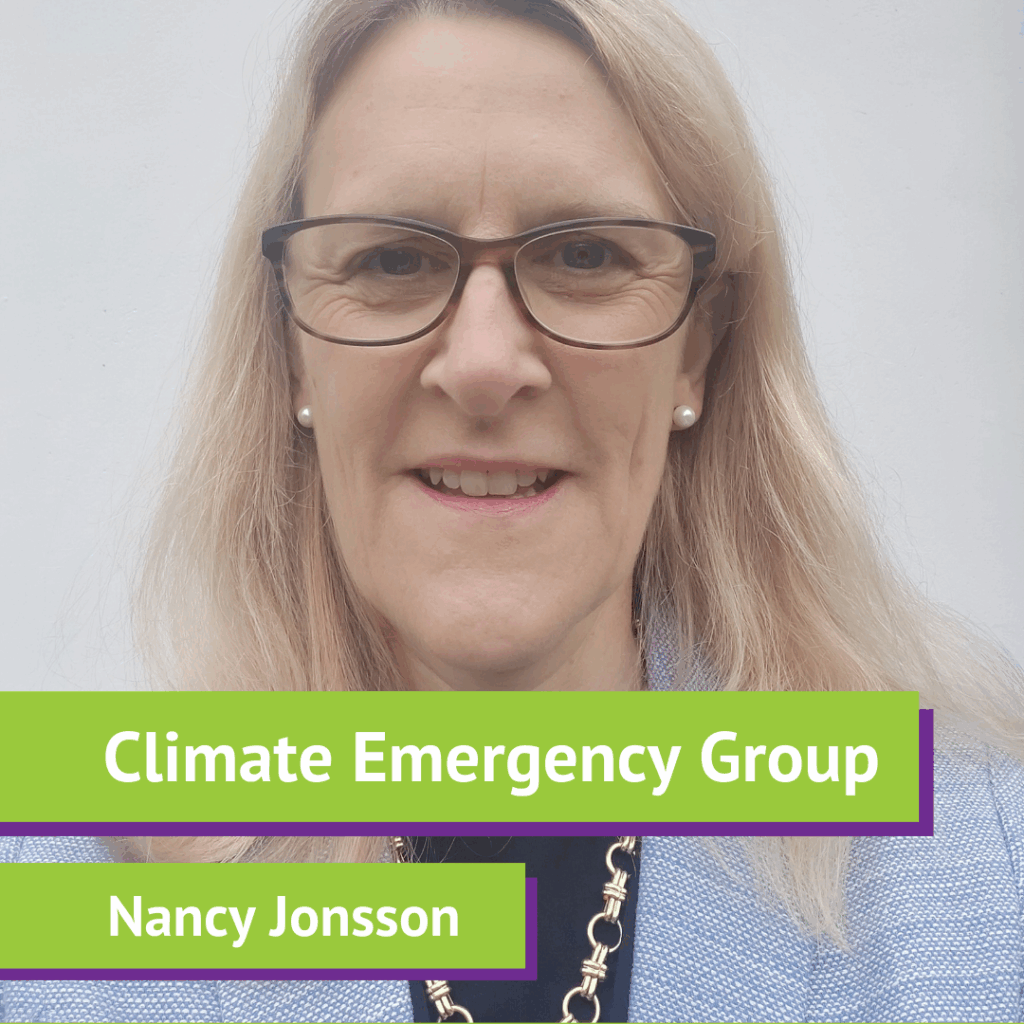 A woman with blonde hair, glasses, and pearl earrings wearing a blue jacket, smiling in front of a plain background, with a green and purple overlay displaying the text "Climate Emergency Group" and "Nancy Jonsson."