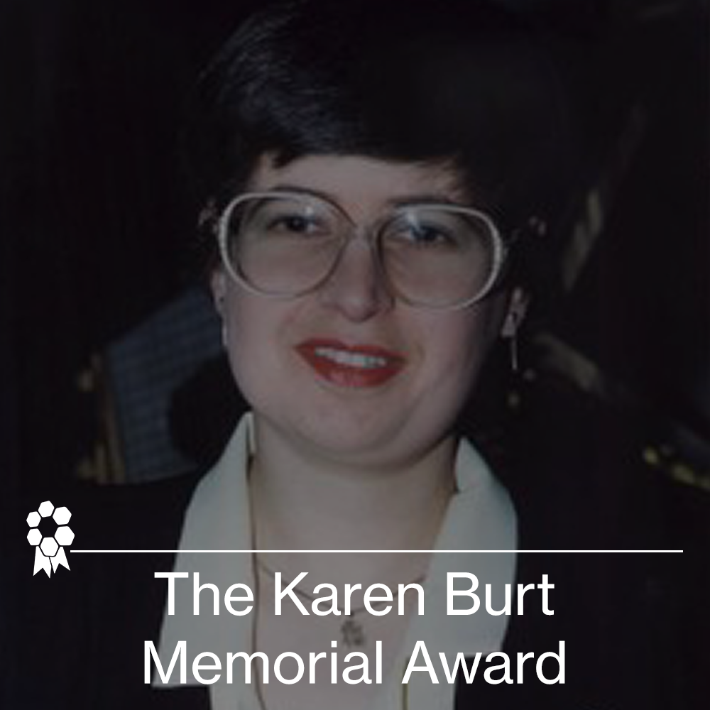 Photograph of a woman with short dark hair, wearing glasses, a white blouse, and a dark blazer, with a medal ribbon and text overlay that reads 'The Karen Burt Memorial Award'.