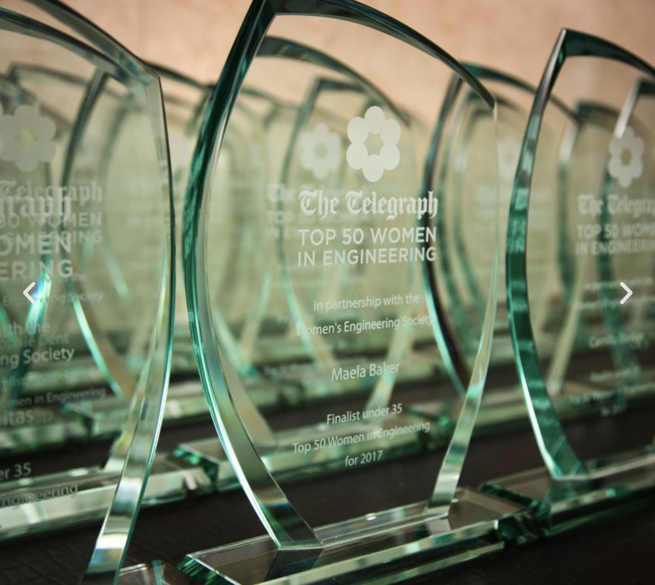Multiple glass awards with engraved text recognizing women in engineering, displayed in a row. The awards are transparent with a greenish tint and have flower-shaped cutouts at the top.