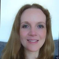 A woman with long, wavy blonde hair and a light complexion smiling at the camera.