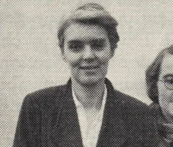 Black and white photo of a woman with short, curly hair, wearing a dark blazer over a light shirt, smiling.