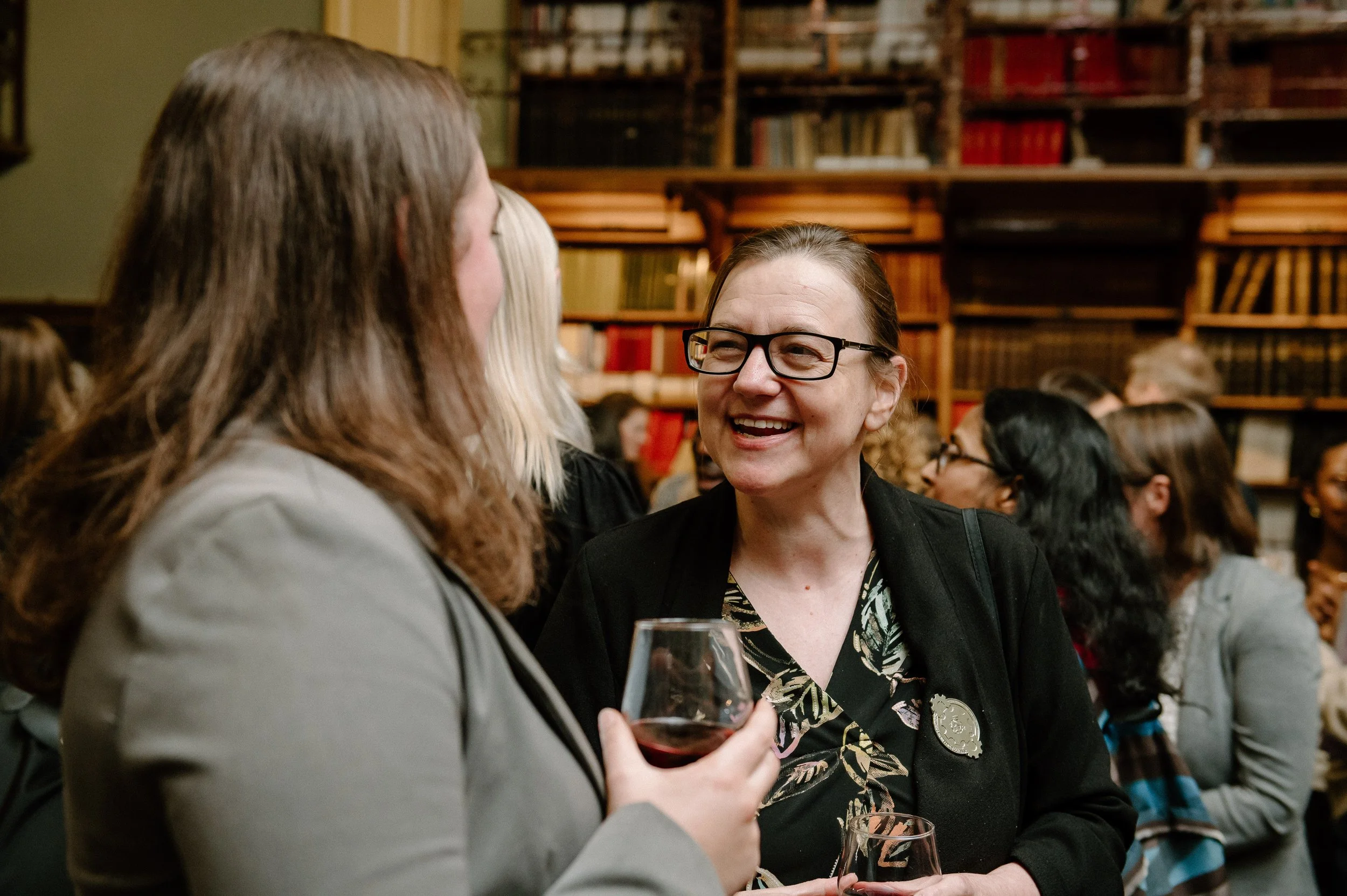 Two women engaged in conversation at an indoor event with a wine glass in one woman's hand.