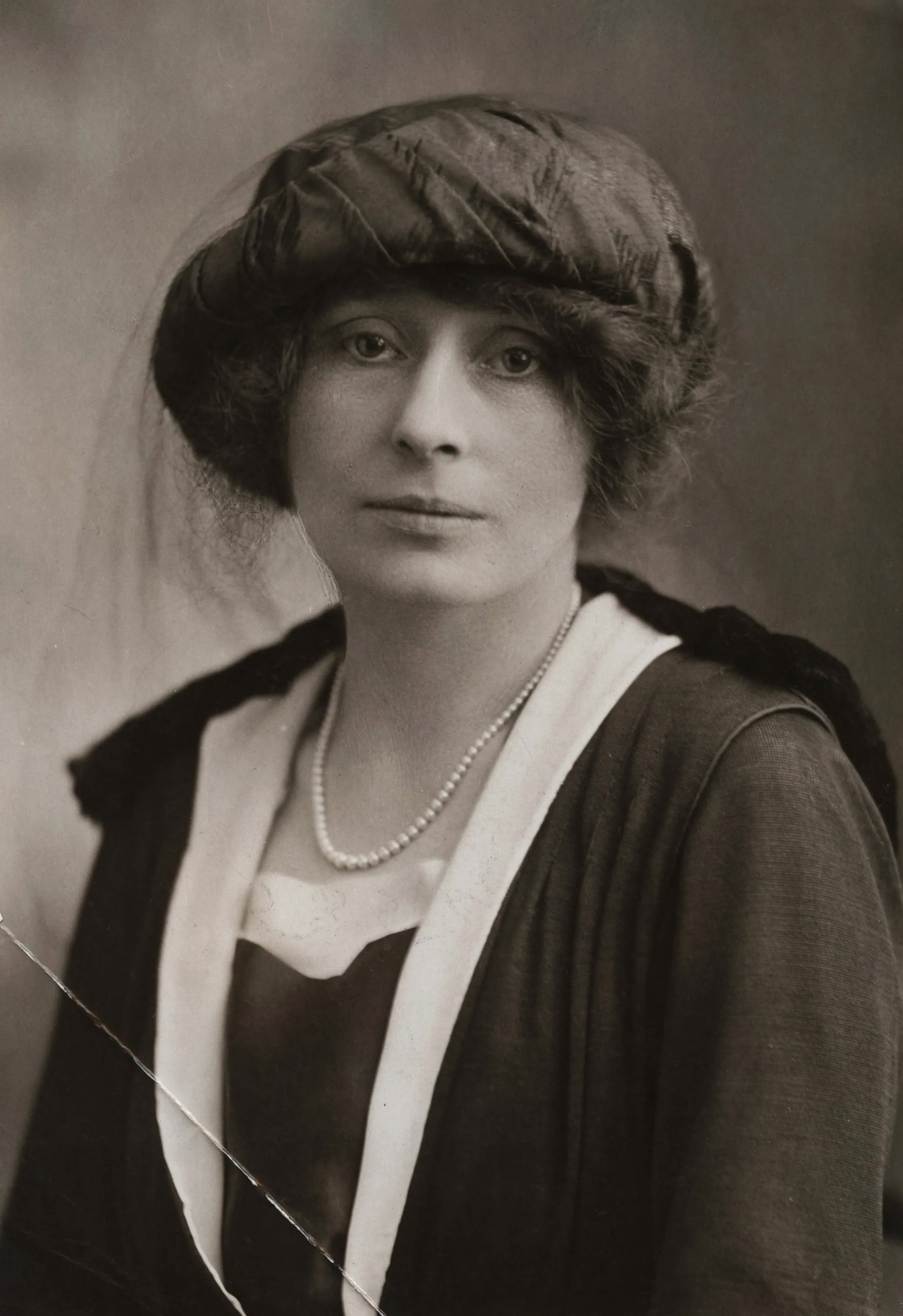Black and white portrait of a woman wearing a headscarf, a white top with black accents, and a pearl necklace.