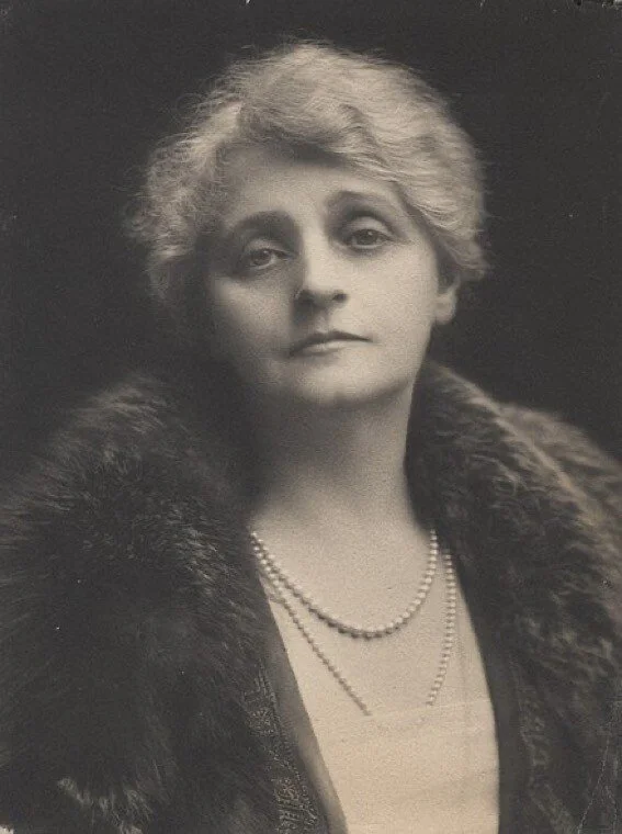 Black and white portrait of a woman with short, wavy hair wearing a fur-collared coat and a pearl necklace.