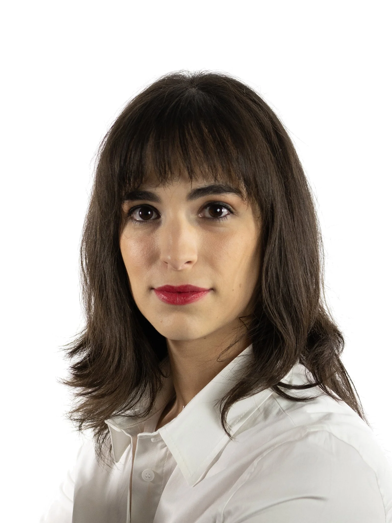 A woman with long, brown hair and bangs, wearing a white button-up shirt, looking directly at the camera with a slight smile.
