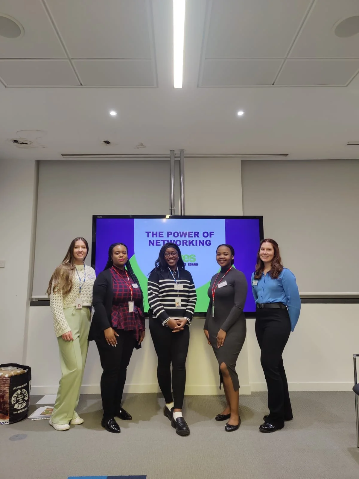 Five women standing in front of a large screen that reads "The Power of Networking" at a conference or seminar, all dressed in business casual attire, smiling for the photo.