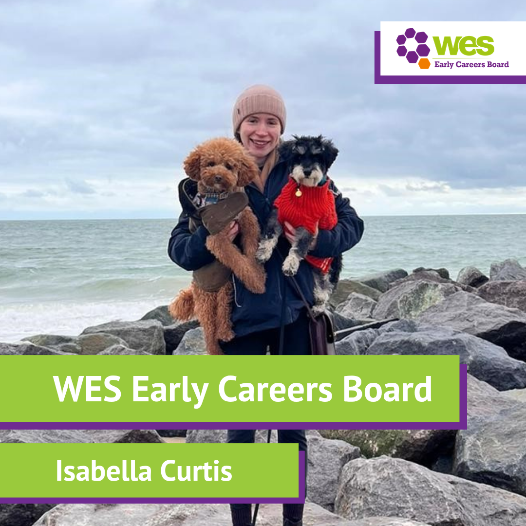 A young woman with a knitted hat holding two small dogs, label states "WES Early Careers Board Isabella Curtis" 