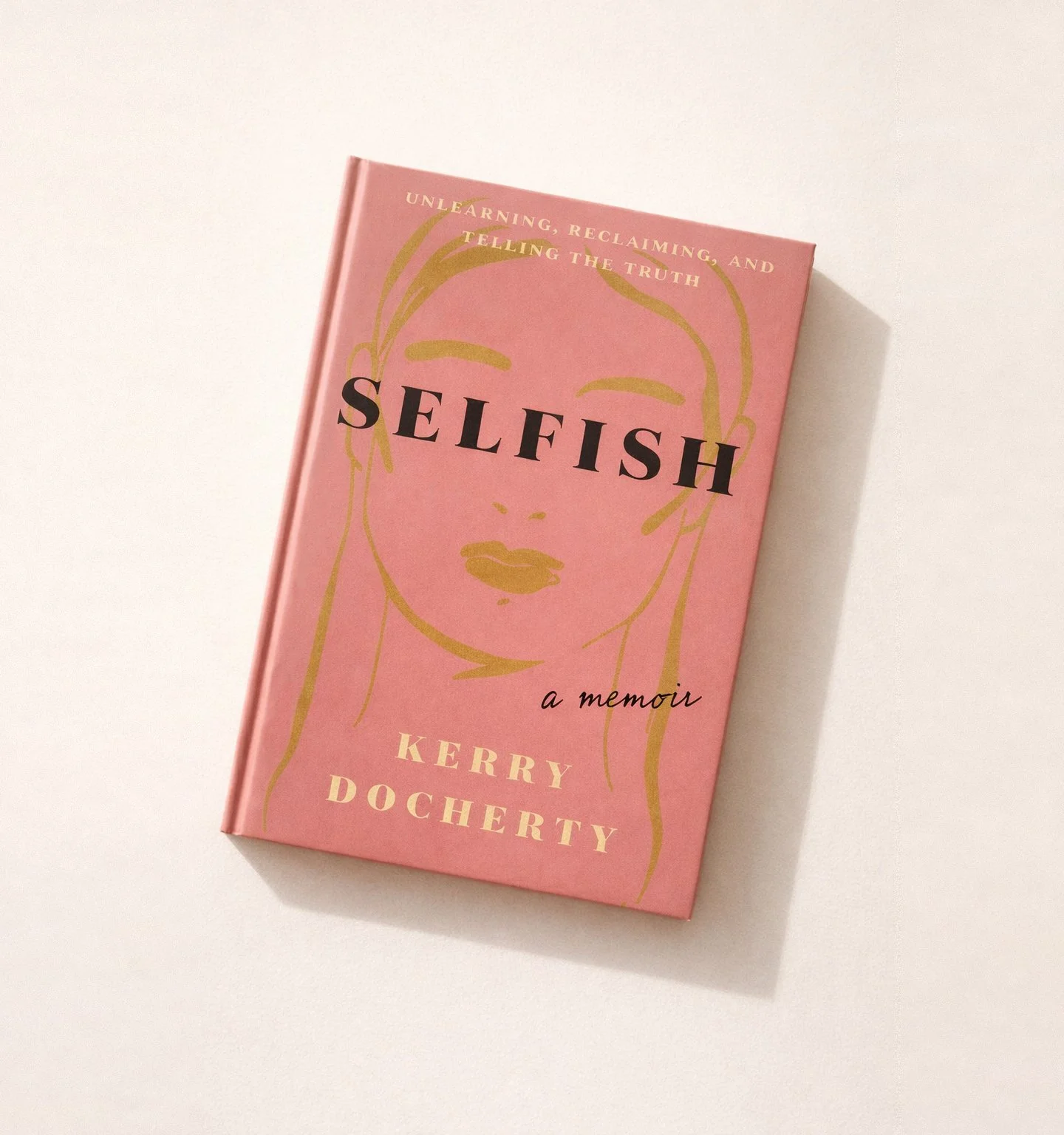 Pink book titled 'Selfish' with gold line art of a woman's face on the cover. Subtitles include 'Unlearning, Reclaiming, and Telling the Truth,' by Kerry Docherty. The book lies on a white surface.