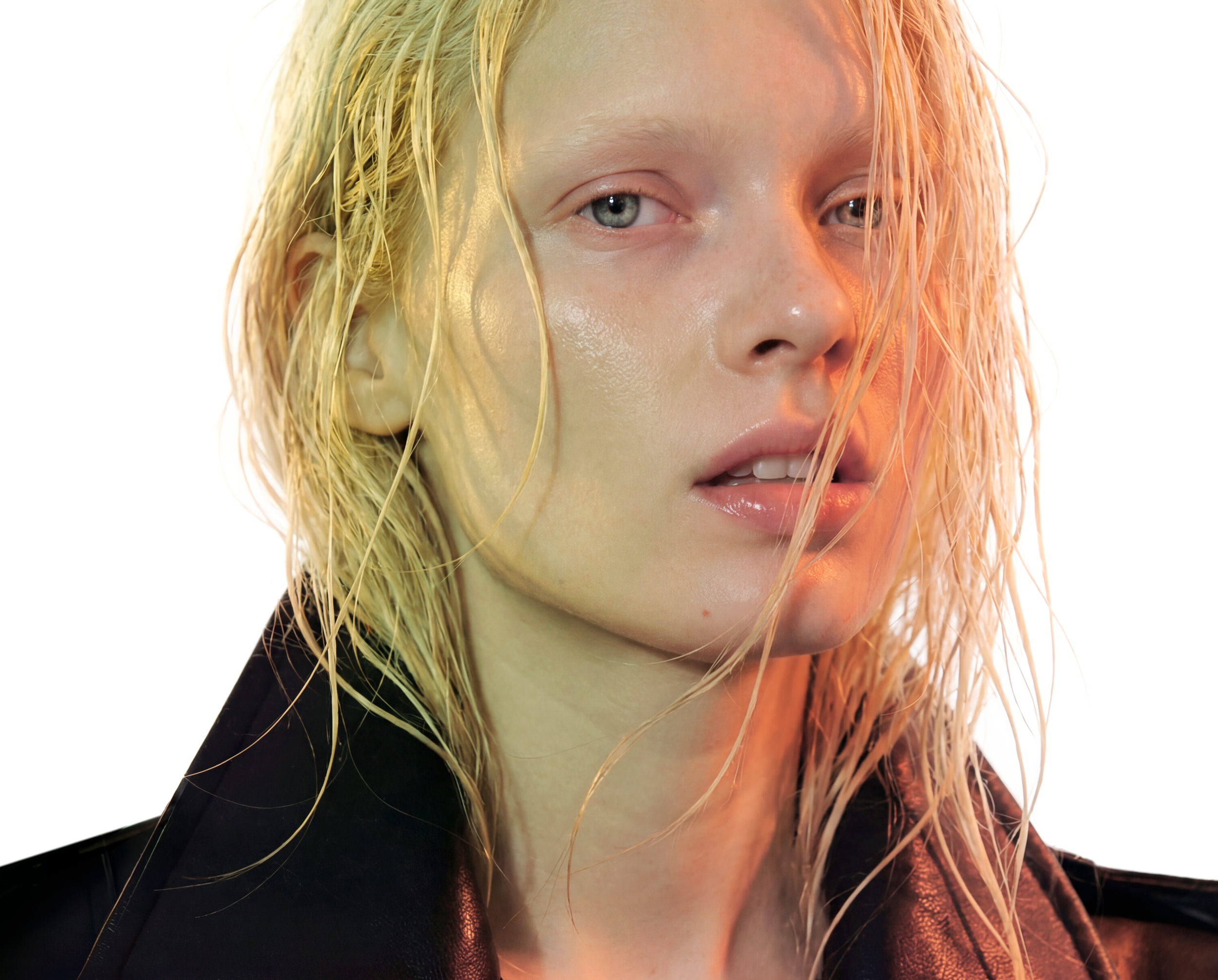 Close-up of a woman with wet blonde hair, pale skin, and blue eyes, wearing a black leather jacket, with warm and cool lighting effects.