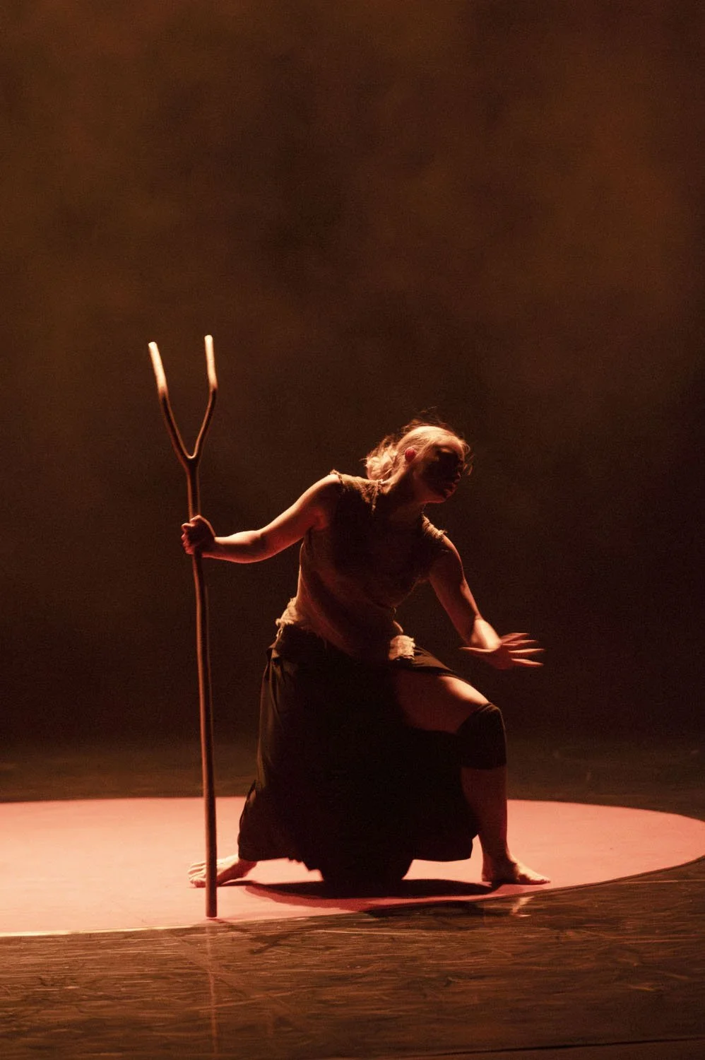 Performer on stage with a trident prop, kneeling on one knee with lighting creating a dramatic atmosphere.