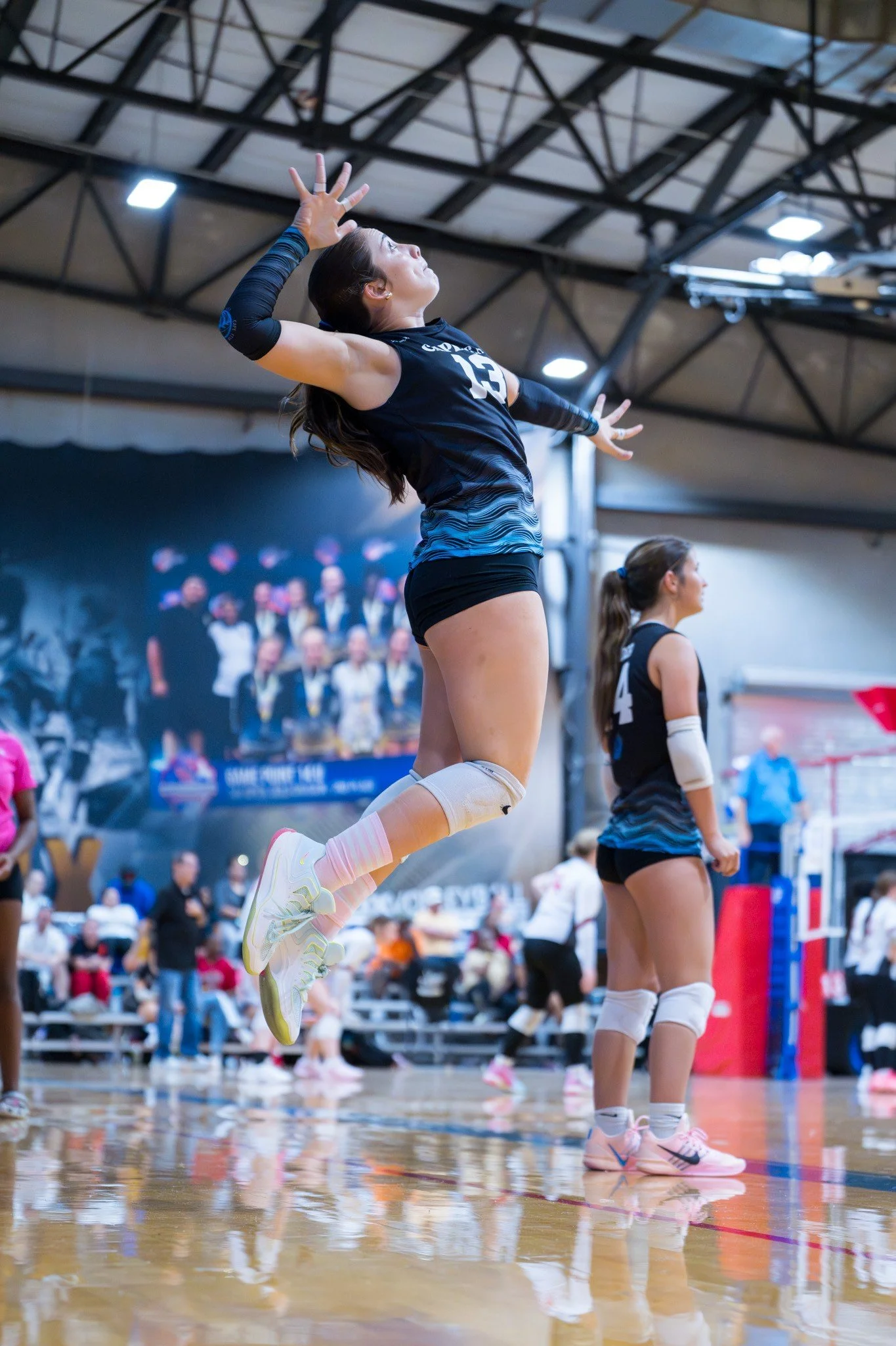 A female volleyball player jumping in the air during a game inside a gymnasium.