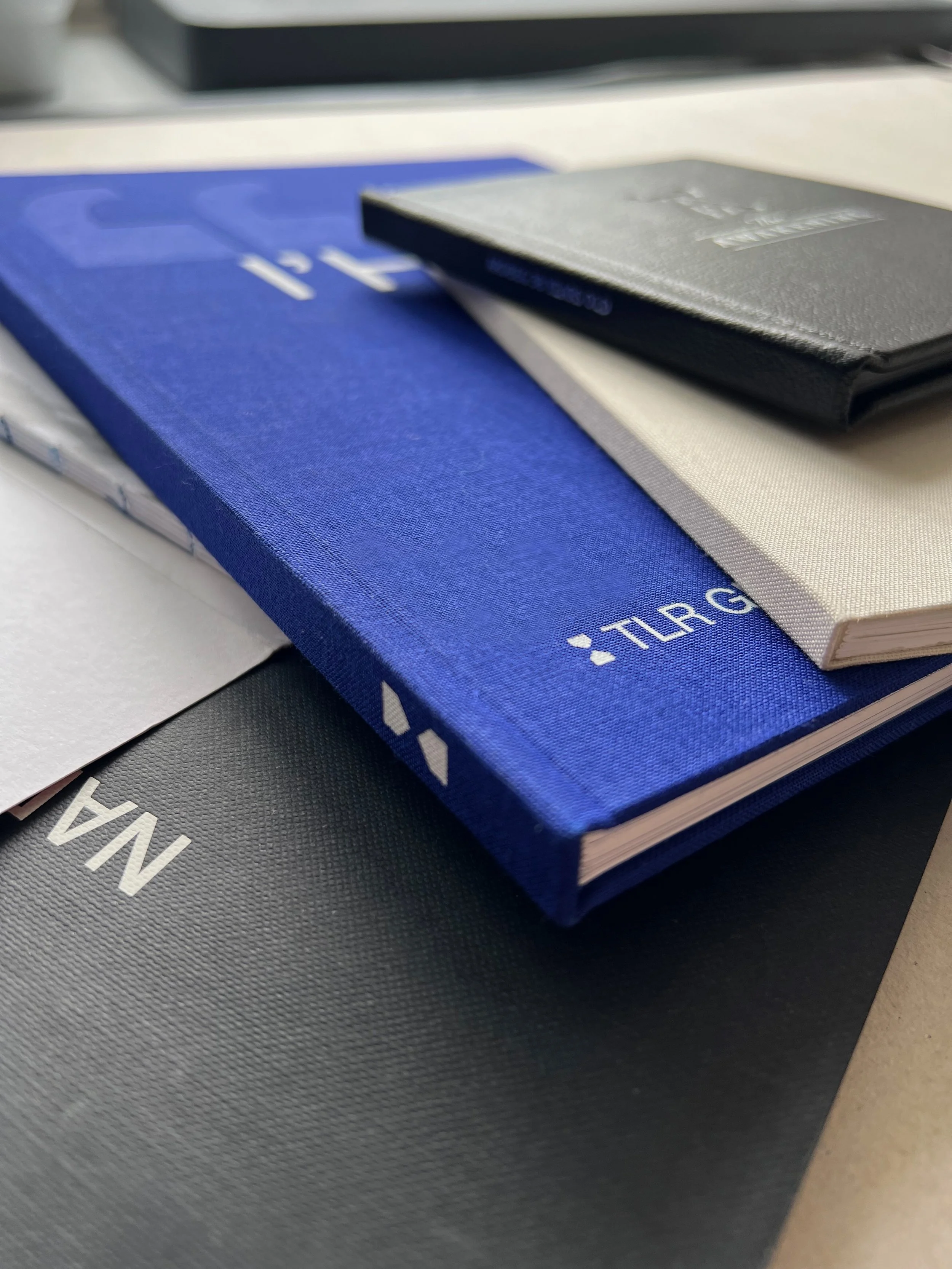 Une collection de cahiers et de blocs-notes empilés, avec différents types de reliures, de papier, de textures (aspect cuir, aspect tissu bleu électrique)