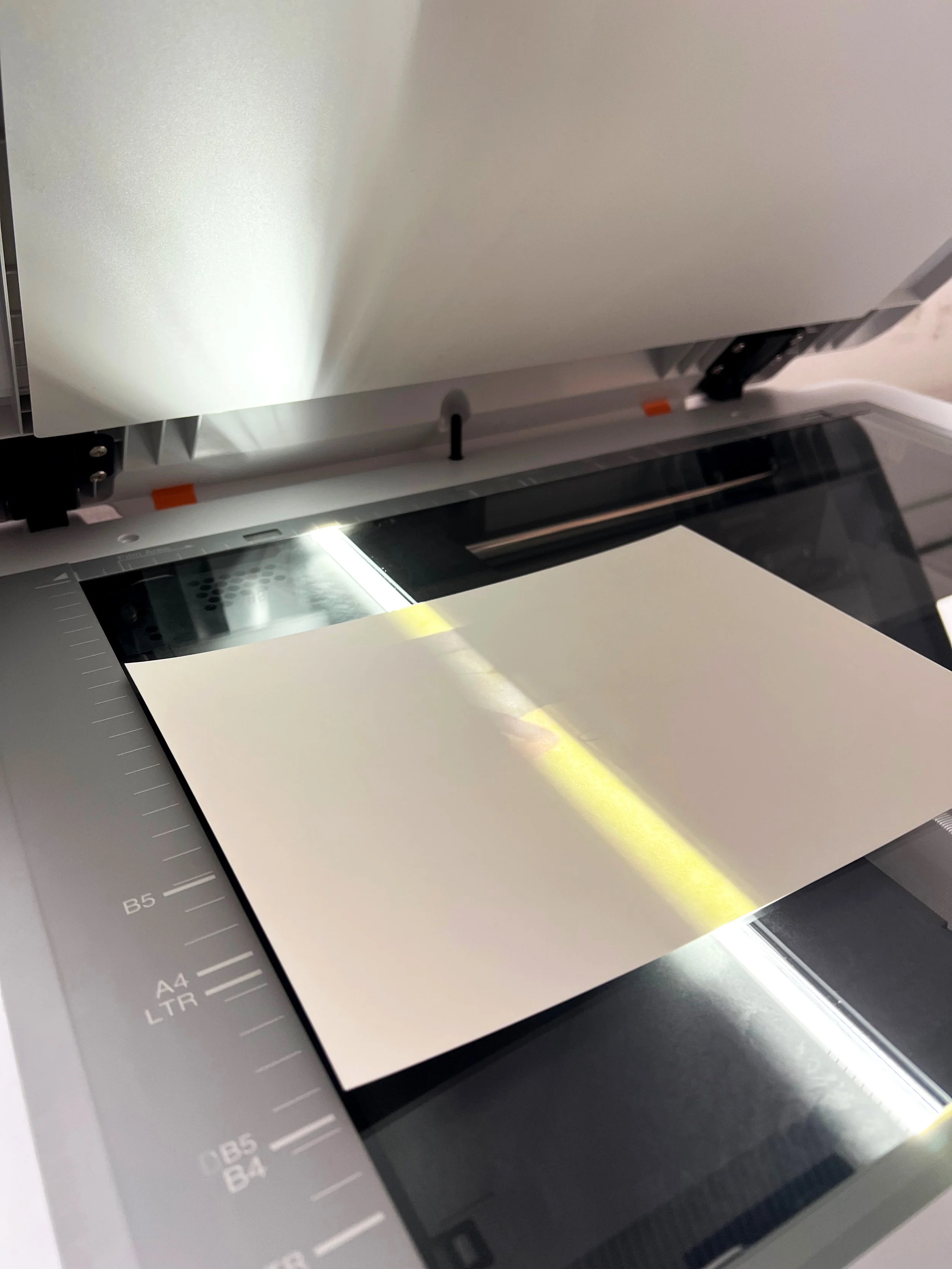 Un scanner professionnel en fonctionnement, avec une feuille de papier sur la vitre sous une lumière vive.