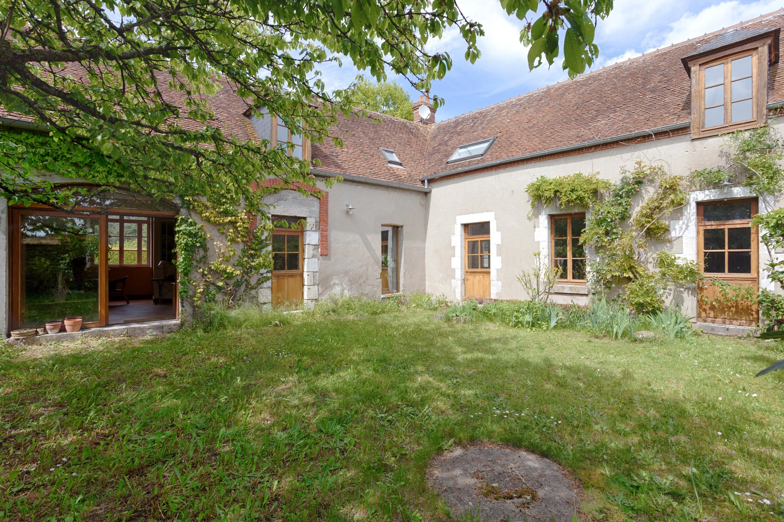 cour intérieure d'une maison en pierre avec un jardin verdoyant, fenêtres en bois avec volets, murs en stuc et toit en tuiles, arbres feuillus