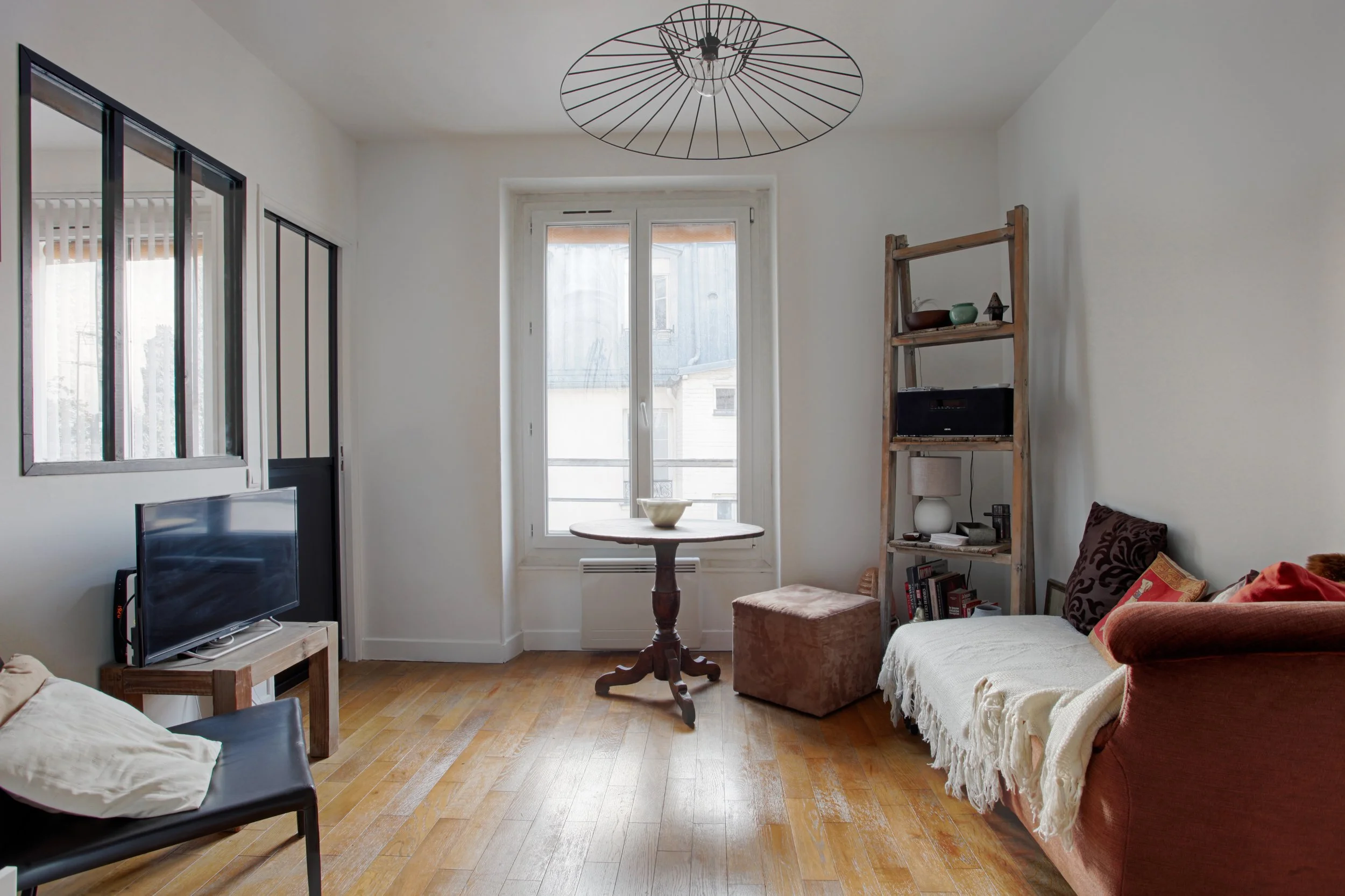 Salon avec fauteuil, canapé, étagère en bois, table ronde, télévision et fenêtre