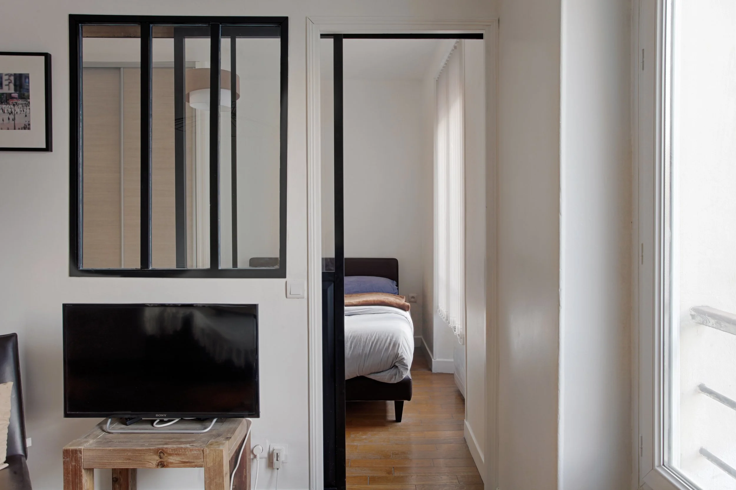 Vue de la chambre depuis le séjour d'un deux pièces avec verrière style atelier