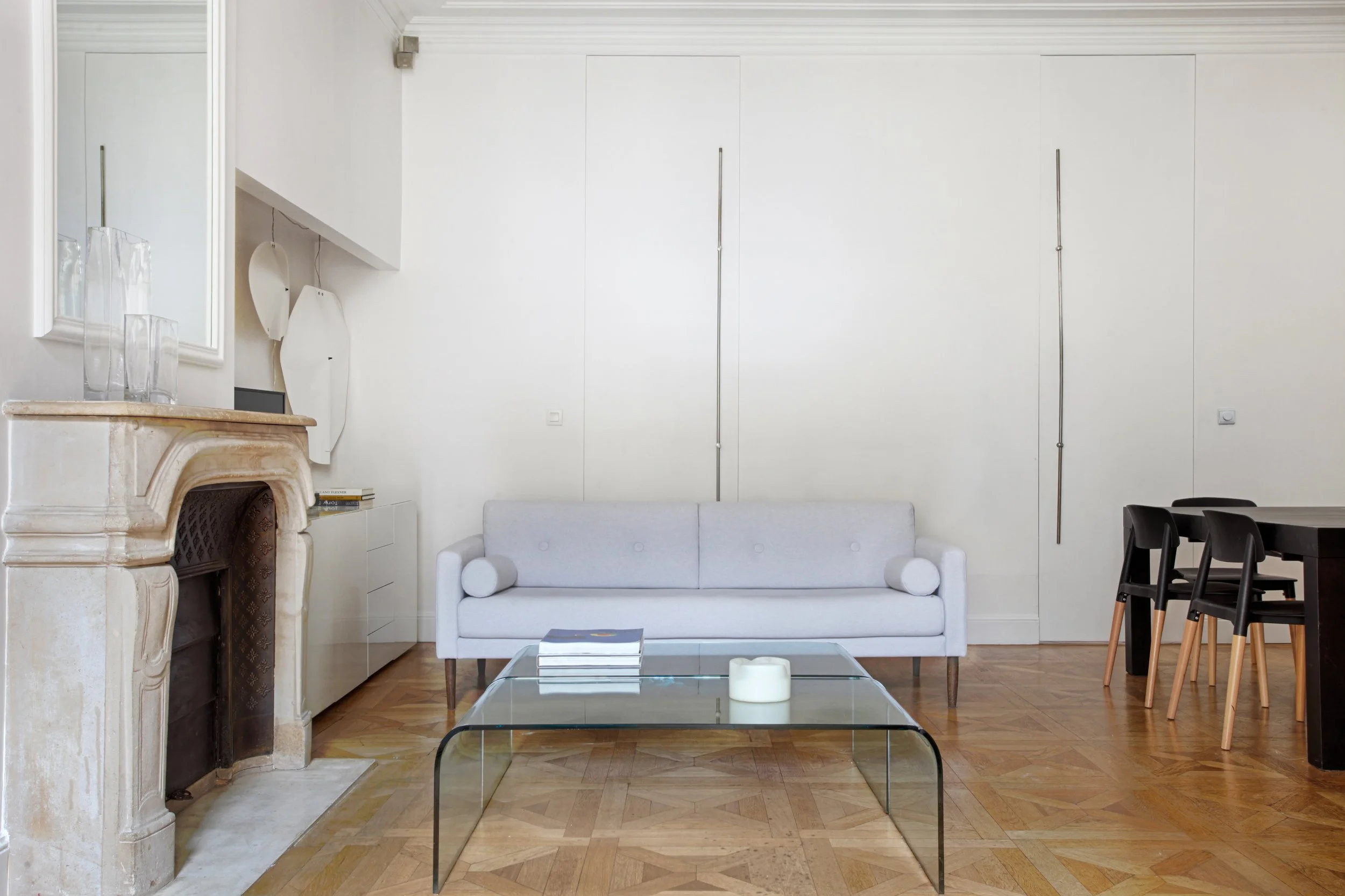 Intérieur d'un salon avec cheminée en pierre, canapé blanc, table en verre, décoration minimaliste, table à manger noire avec chaises en bois.