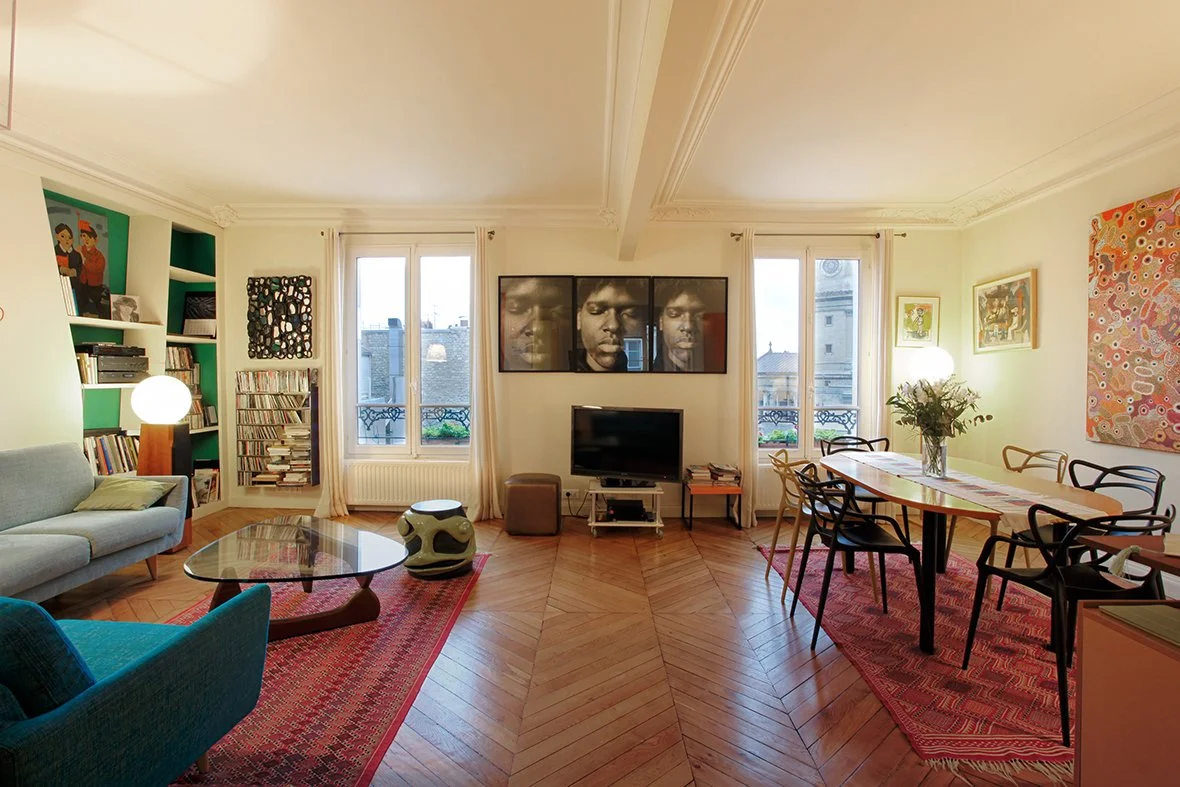 Salon lumineux avec livres, télévision, œuvres d'art et table à manger avec fleurs.
