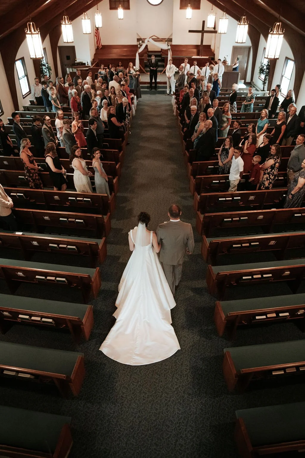 Bride and groom walking down the aisle at their wedding ceremony in a church, with guests seated on both sides of the aisle and clergy at the altar in the background.