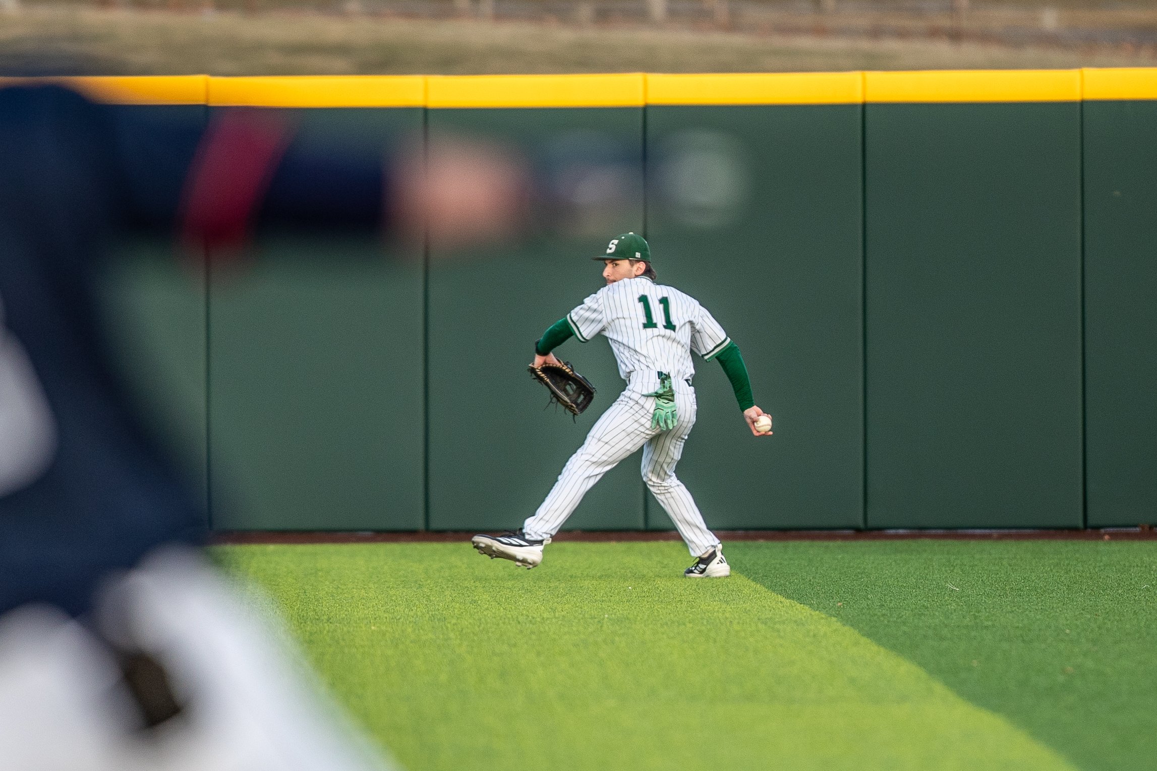 A baseball player wearing a uniform with the number 11, preparing to catch a ball near the outfield wall.