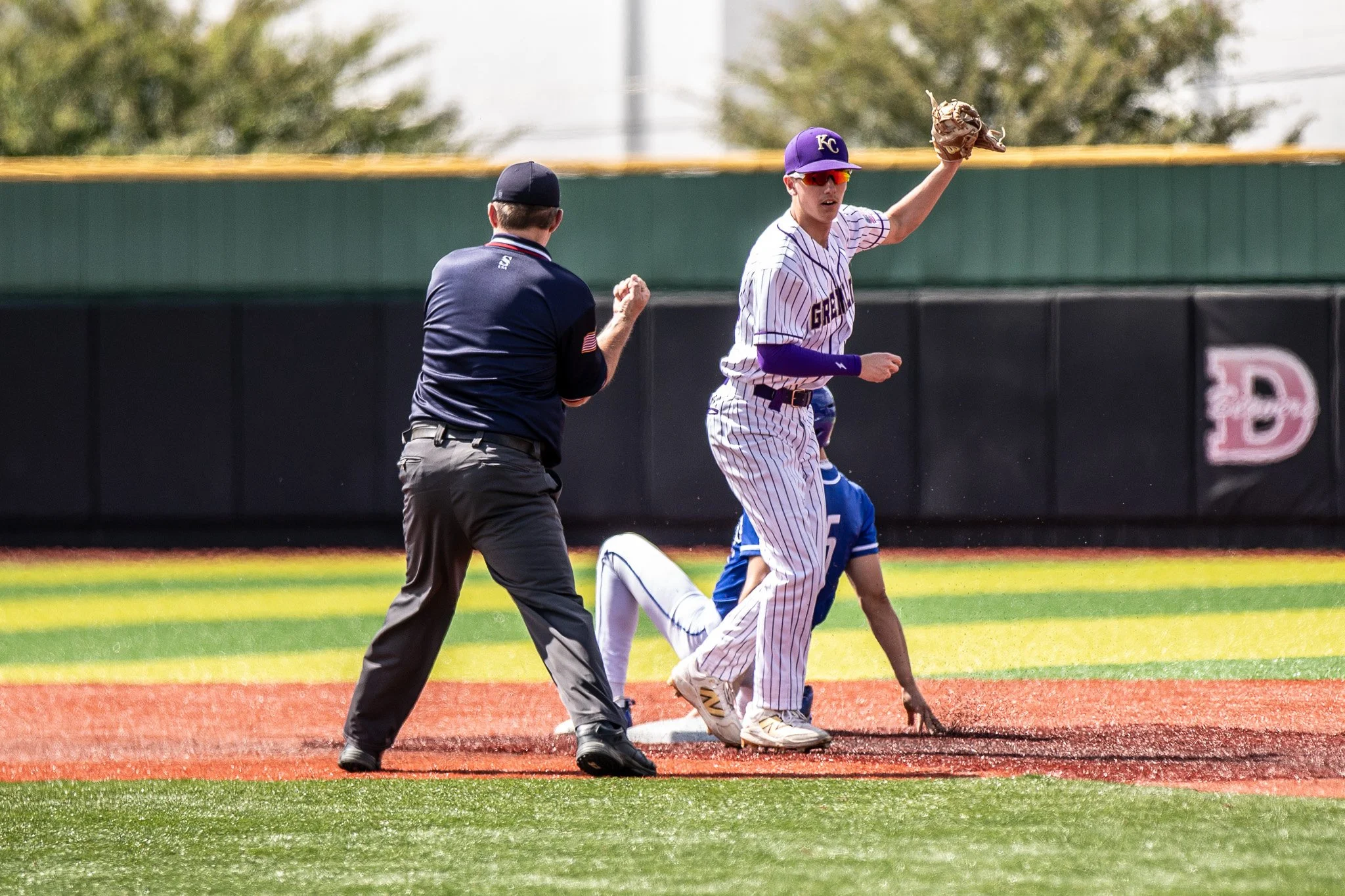 A baseball player from the Kansas City team catches a ball while standing on second base during a game, with an umpire nearby and another player on the ground.
