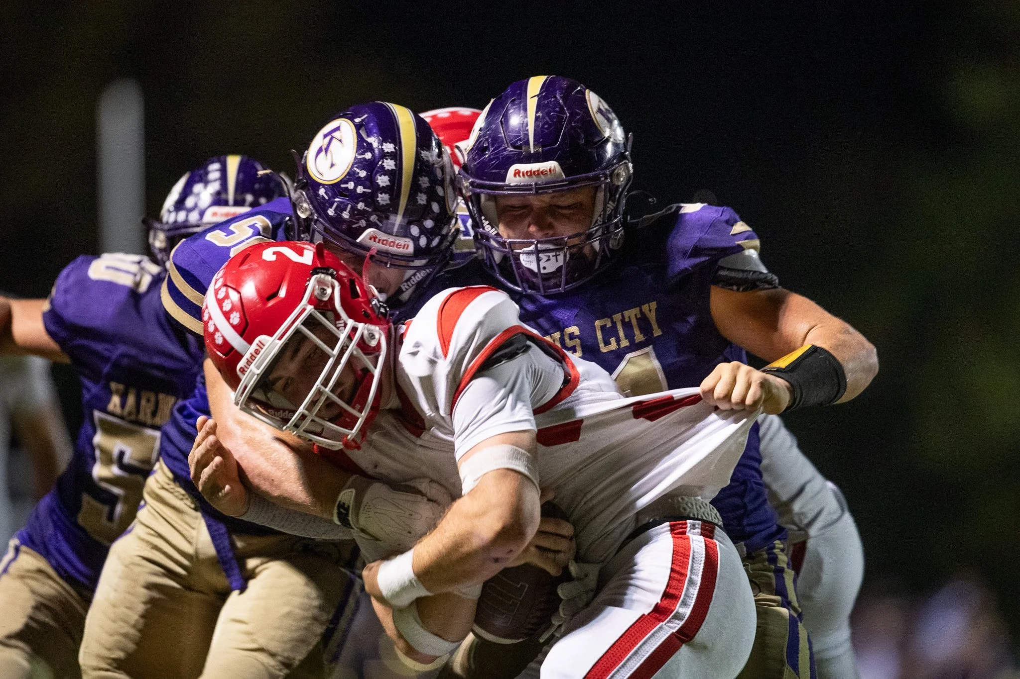 The ball carrier gets tackled by 3 defenders in a high school football game.