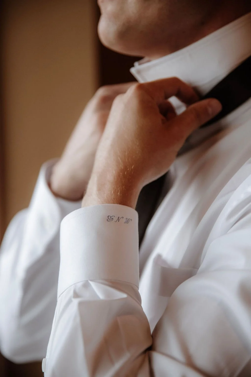 Close-up of a man adjusting his black bow tie while wearing a white dress shirt, with part of his face and hand visible.