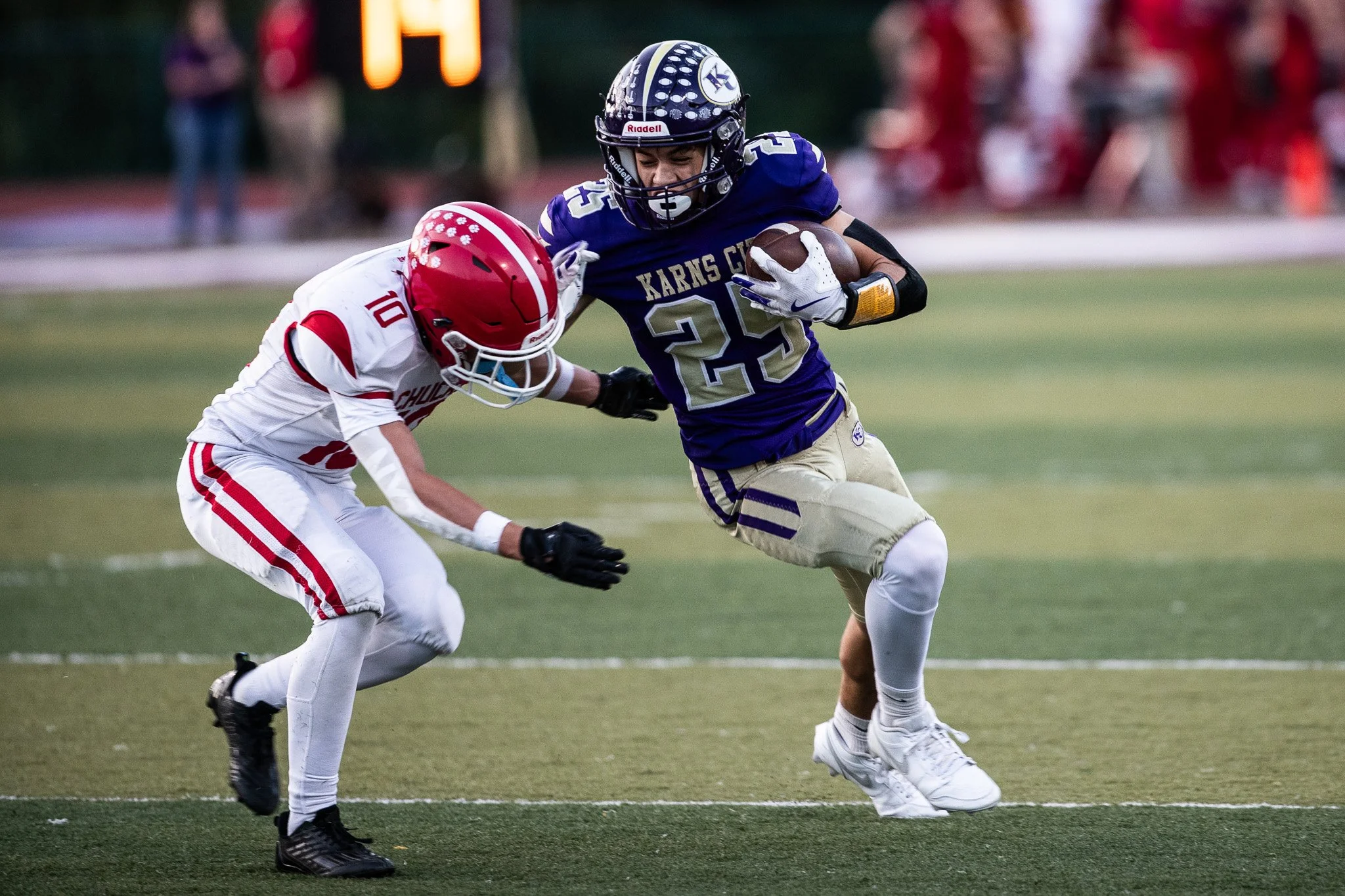 Two football players in action during a game, one in a blue uniform and the other in a white and red uniform, with the player in blue running with the ball.