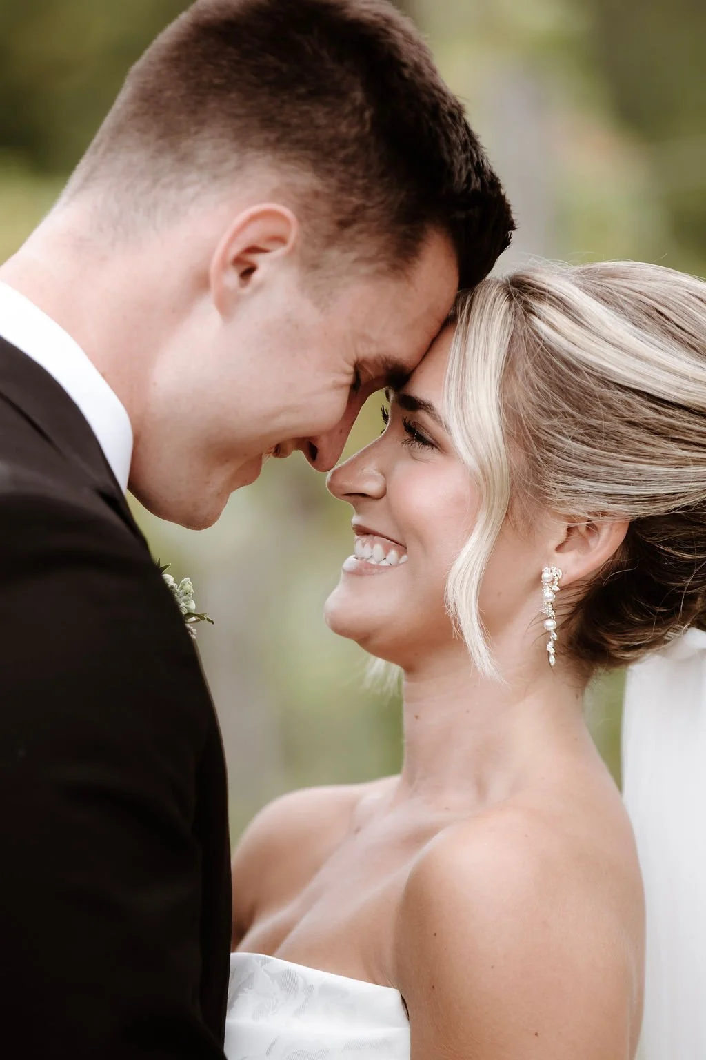 A bride and groom with foreheads touching and smiling at each other during their wedding.