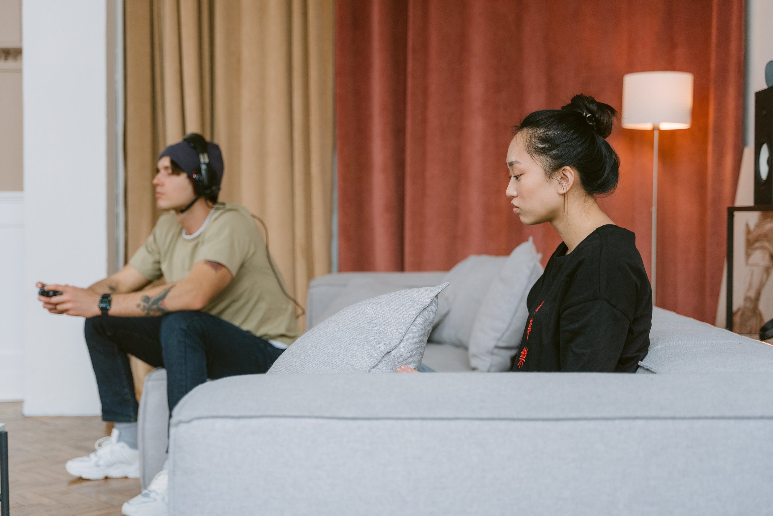 Couple sitting on opposite ends of a couch, each focused elsewhere