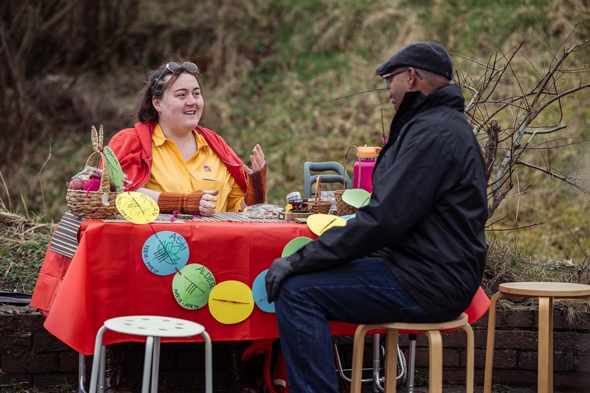Two people sat at table talking outdoors.