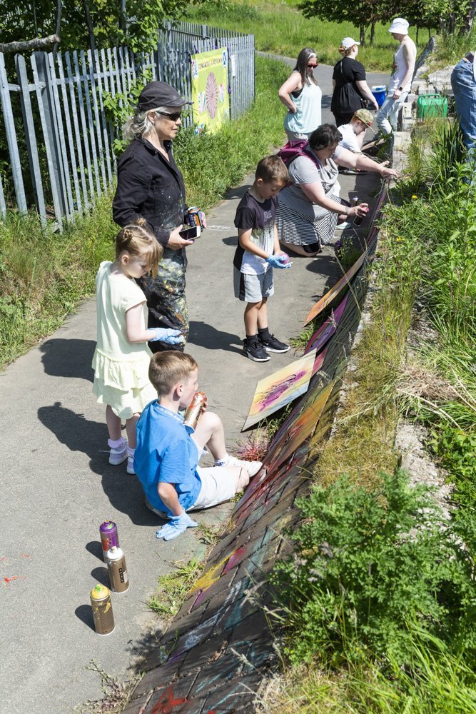 Community participants looking a pieces of artwork against hedge.