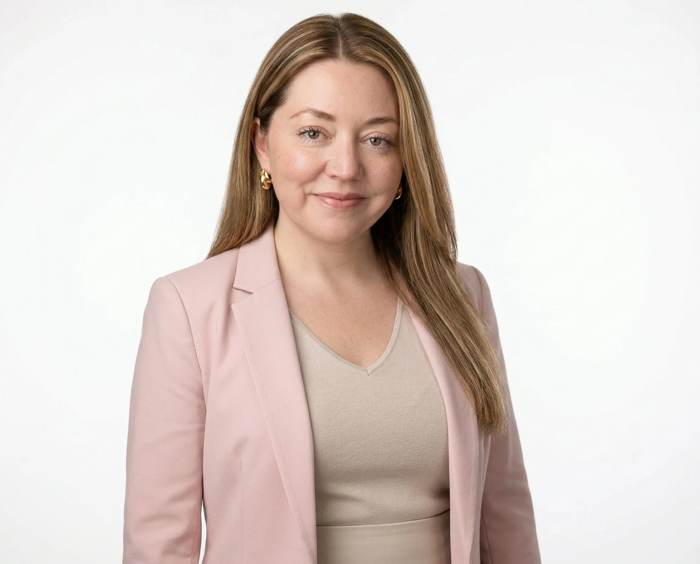A woman with light brown hair, wearing a pink blazer and a beige top, smiling against a white background.