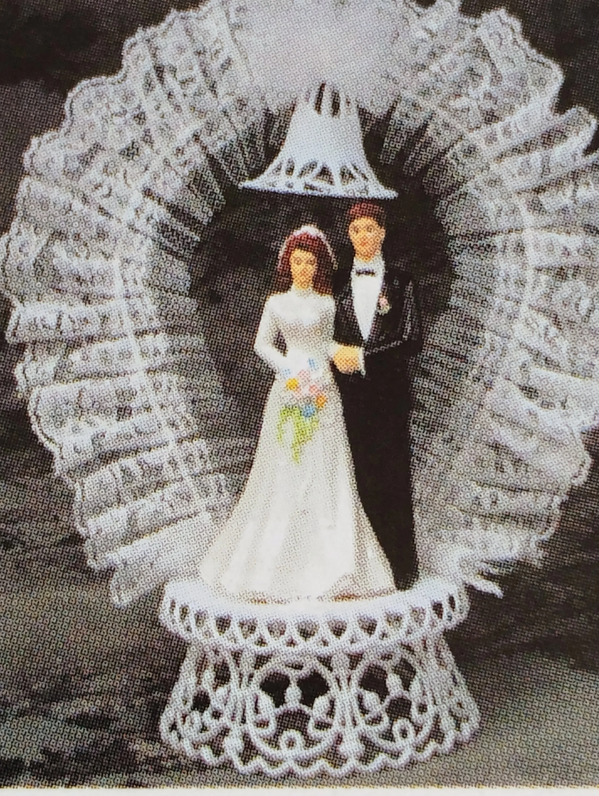 A pair of bride and groom figurines inside a decorative lace frame with a lace lace background.