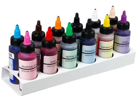 Array of colorful airbrush paint bottles on a white stand, each labeled with different colors such as blush pink, super red, spring green, hawaiian blue, canary yellow, violet, and more.