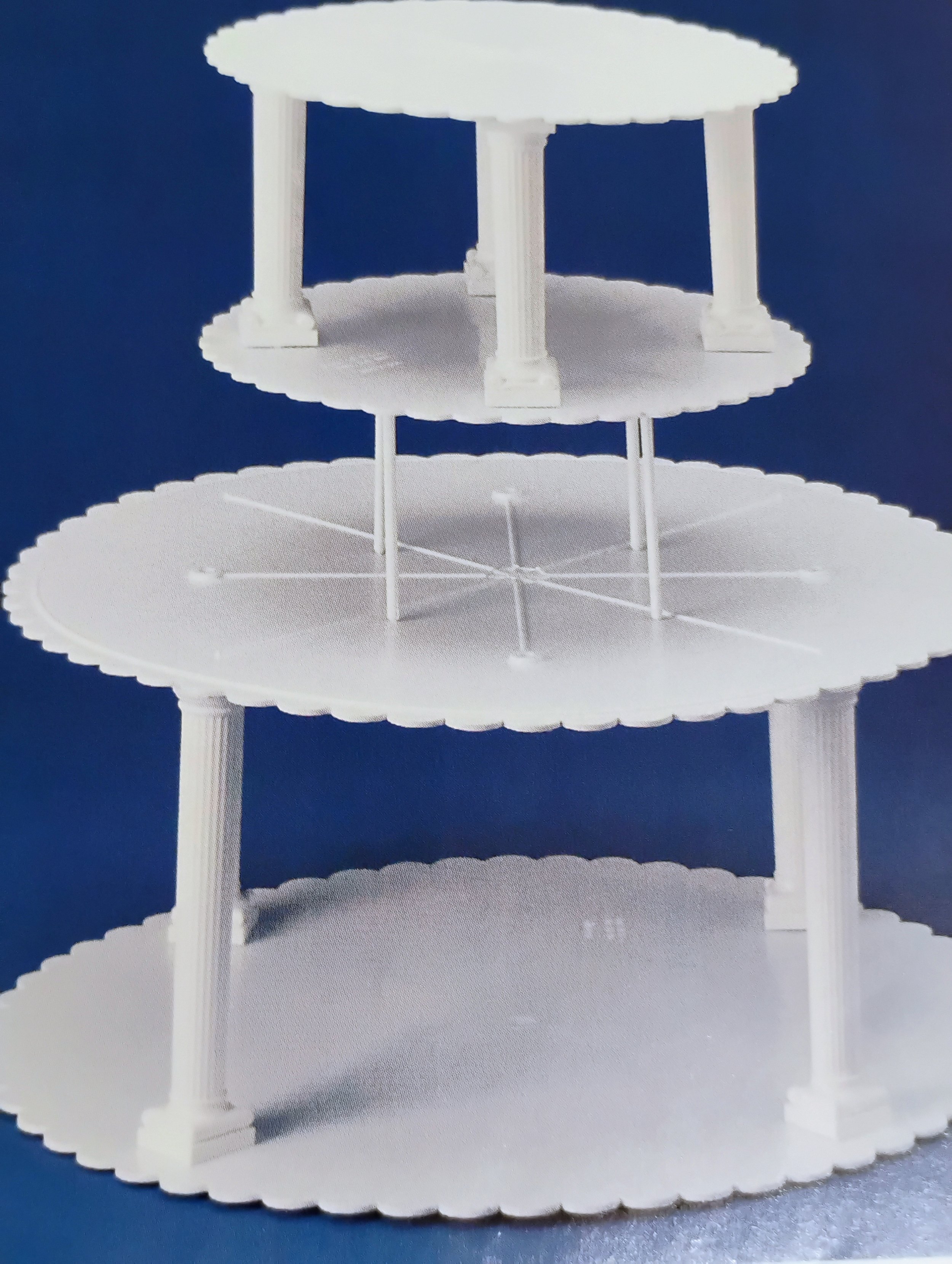 A three-tiered white plastic cupcake stand with four columns supporting each tier, set against a blue background.