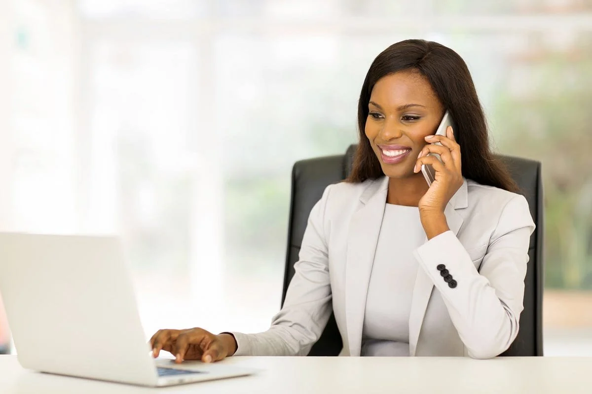 Businesswoman smiling while talking on the phone at her desk with a laptop.
