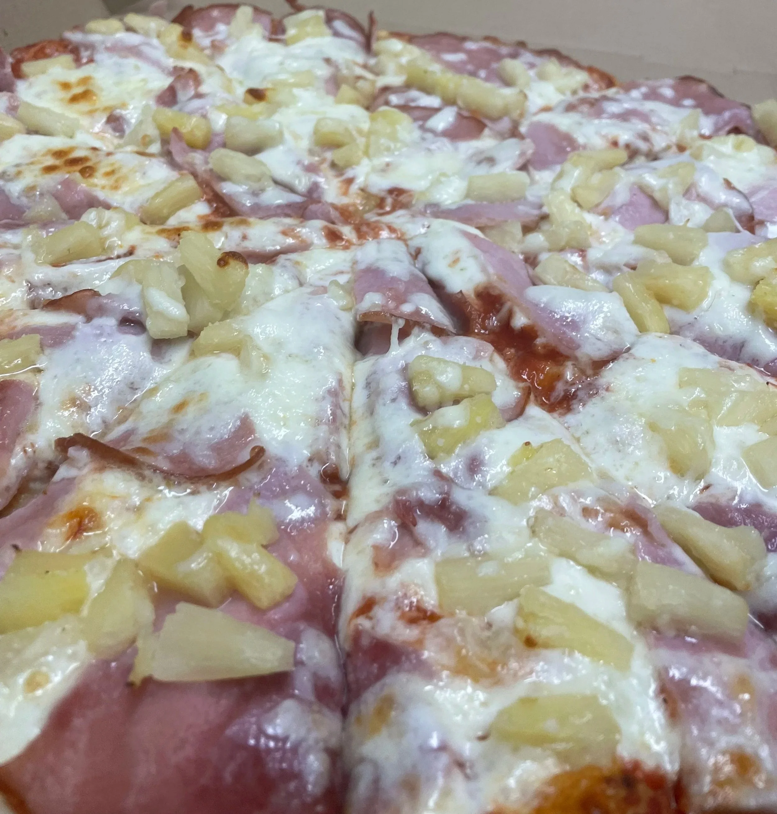 Close-up of a pizza with cheese, pineapple pieces, ham, and possibly some other toppings.