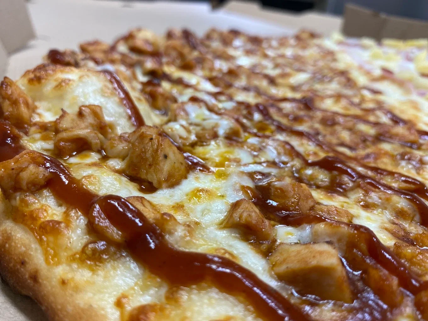 Close-up of a pizza with chicken, cheese, and barbecue sauce on a pizza crust.