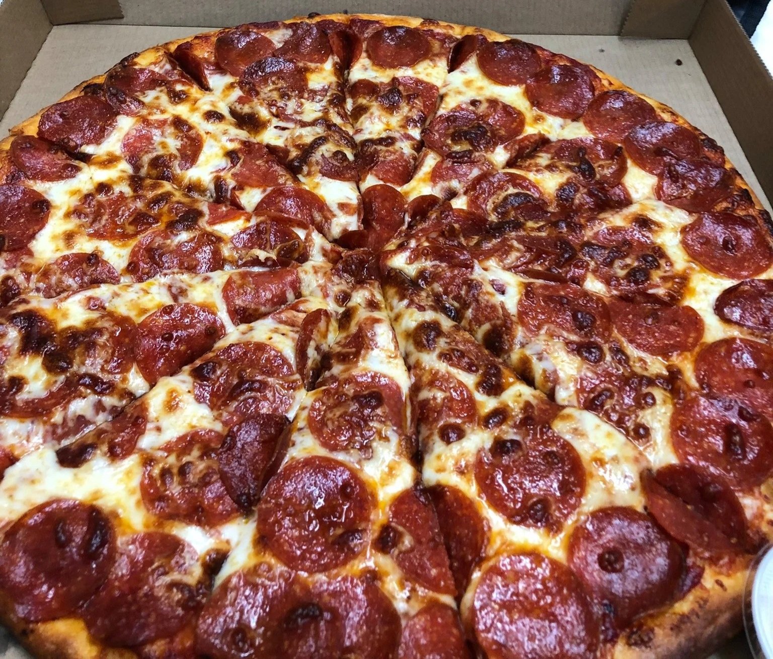 Large pepperoni pizza in an open cardboard box with a golden crust and melted cheese.