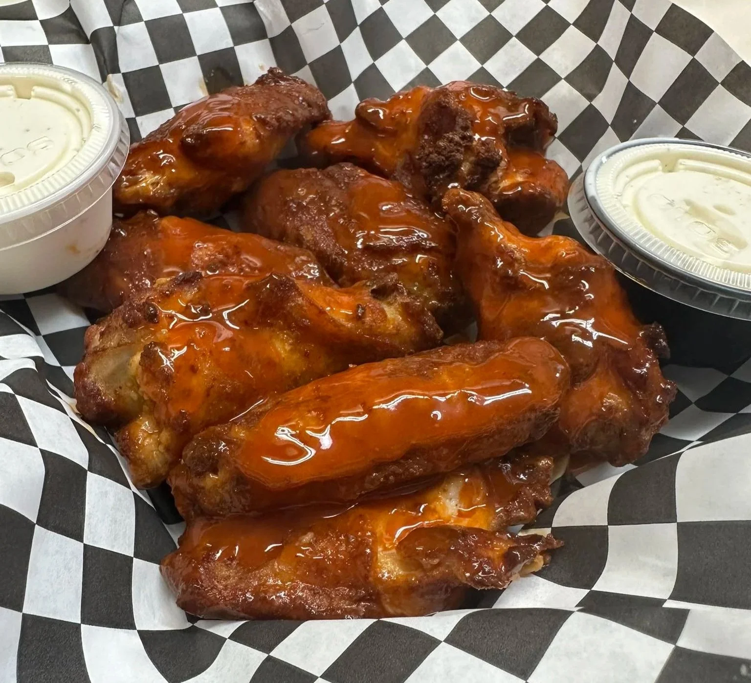 A basket of glazed chicken wings with two small containers of dipping sauce, one on each side.