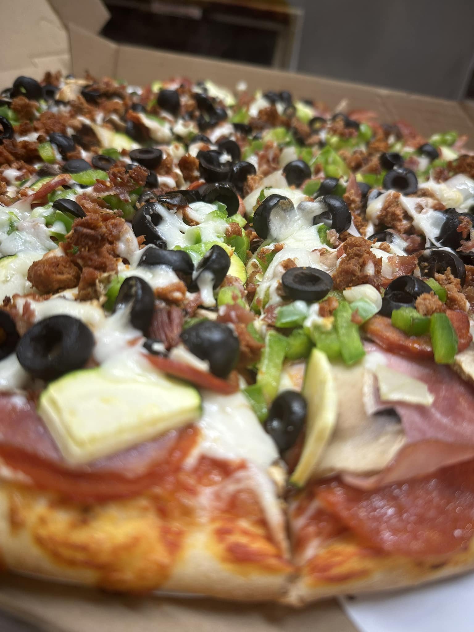Close-up of a pizza with black olives, green peppers, pepperoni, and melted cheese.