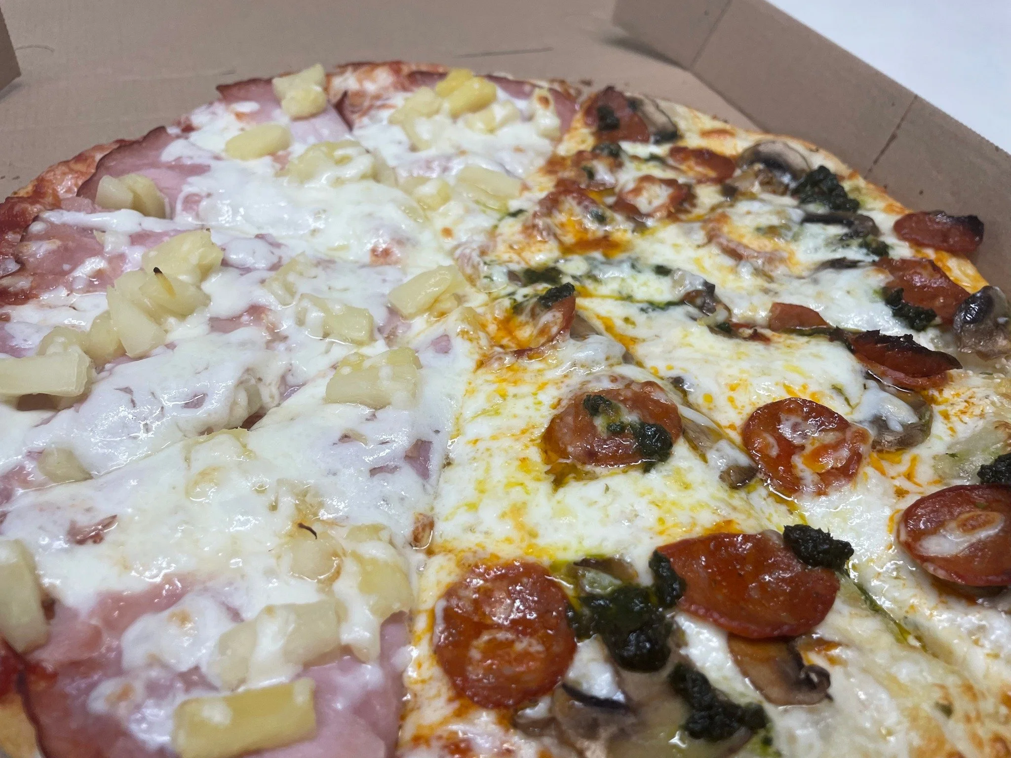 Close-up of a half pepperoni and mushroom pizza in an open box.