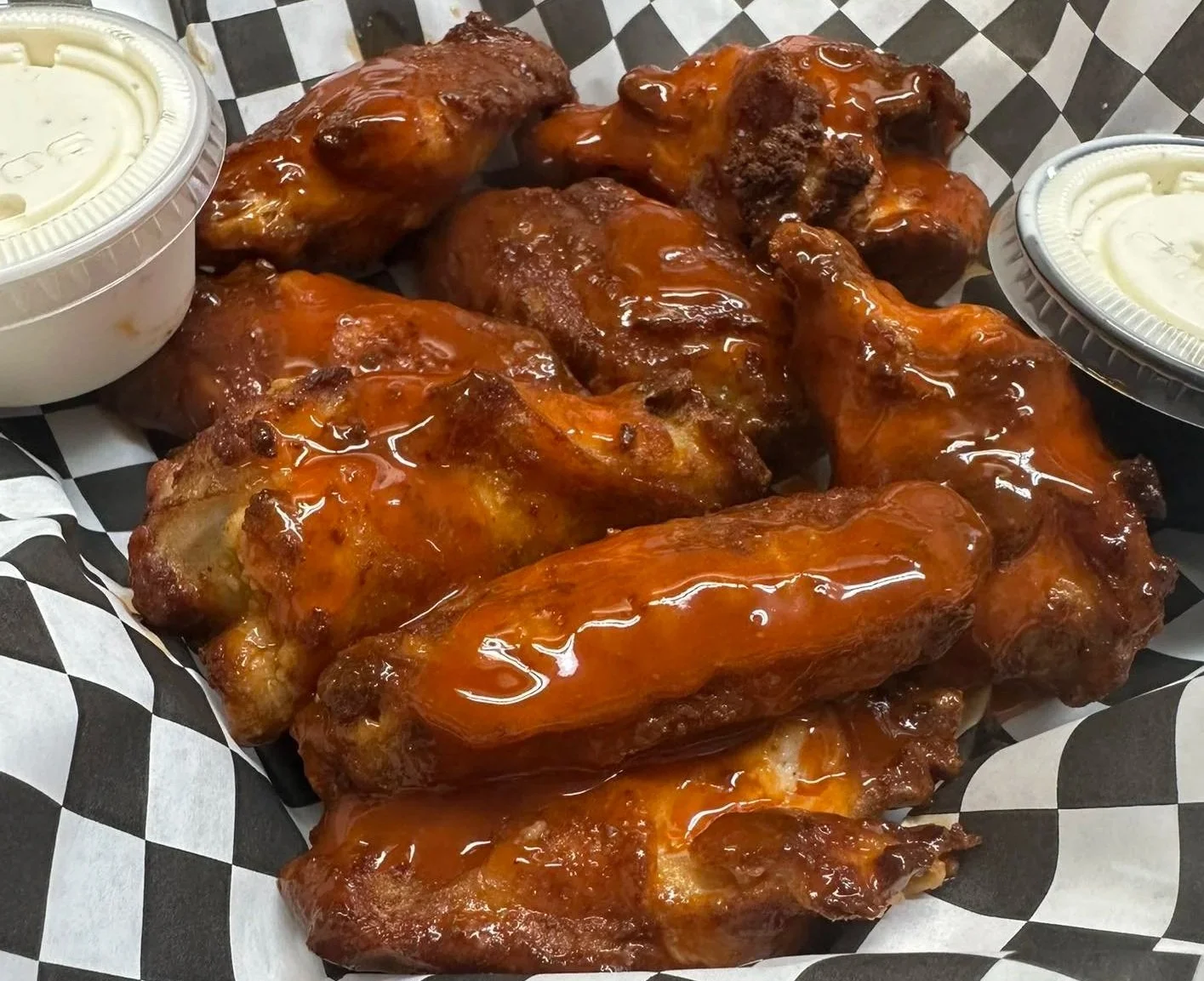 A basket of saucy buffalo chicken wings with two containers of dipping sauce on the sides.