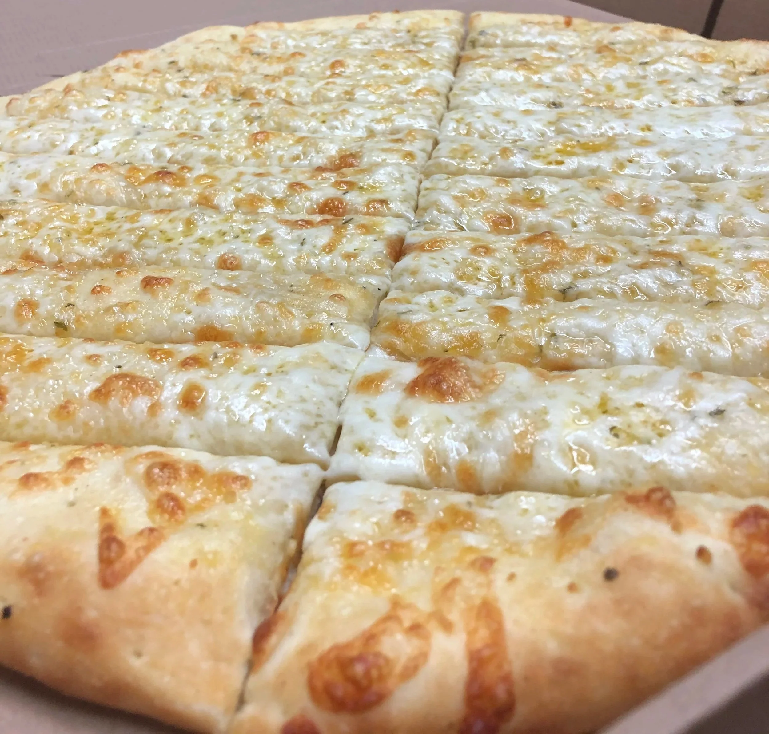 Close-up of a cheese pizza sliced into squares with melted cheese and a golden-brown crust.