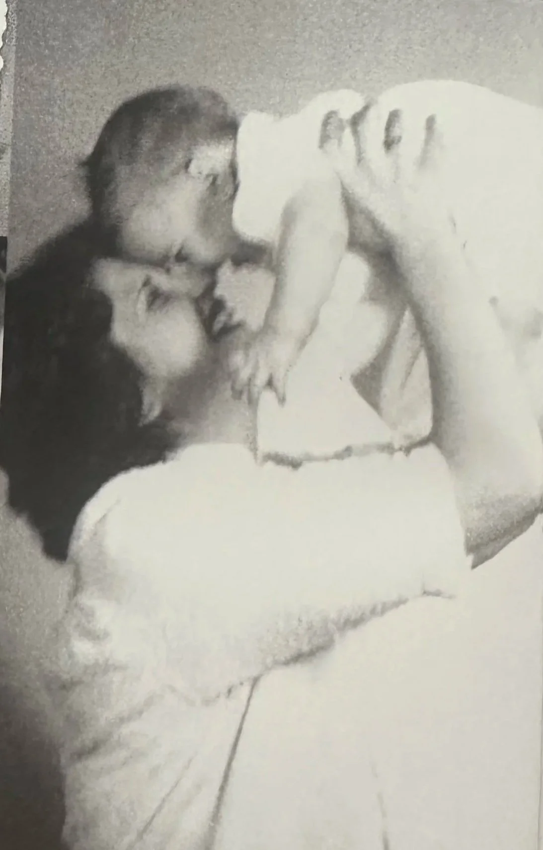 A black and white photo of a man and a young girl sharing a kiss while a baby sits nearby, looking at them.