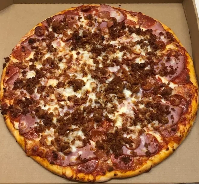 A pizza with a golden crust topped with pepperoni, sausage crumbles, and ham, on a cardboard pizza box.