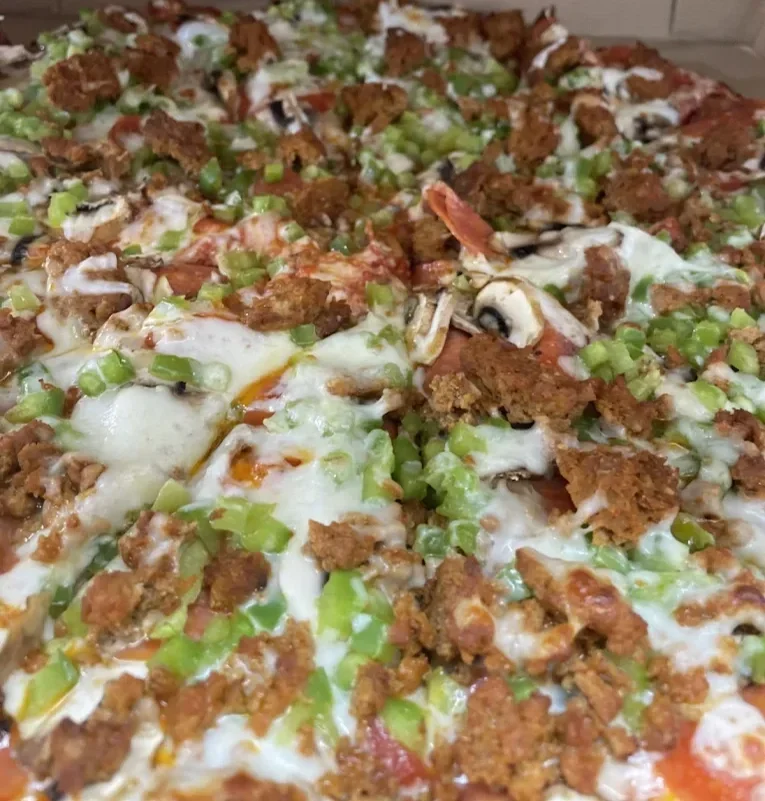 Close-up of a pizza with crumbled sausage, green onions, mushrooms, and melted cheese.