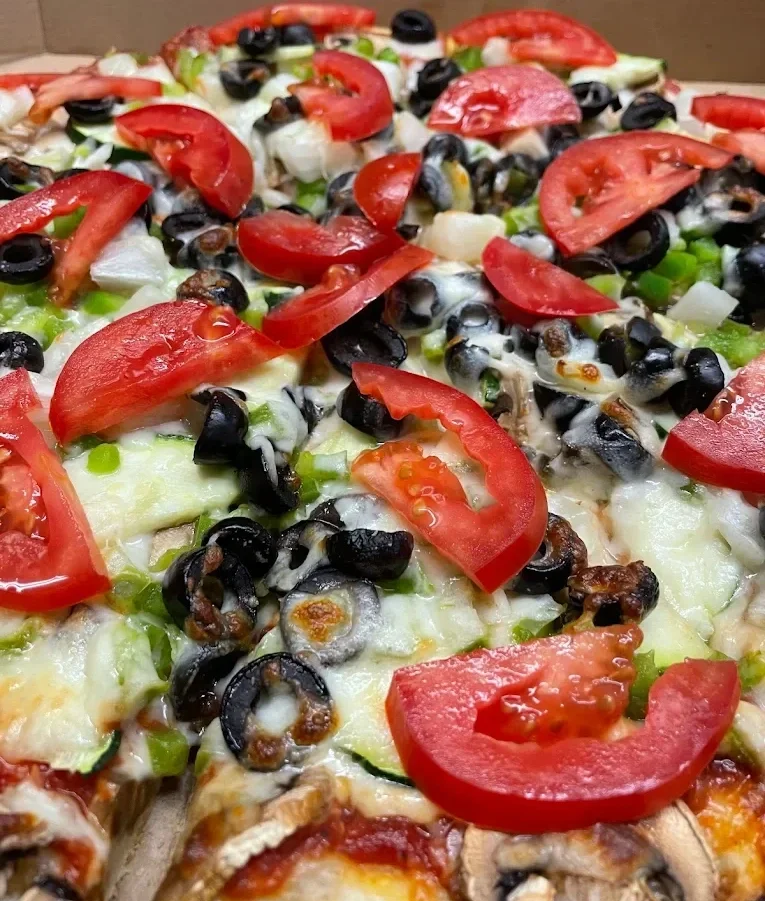 Close-up of a freshly baked pizza topped with sliced tomatoes, black olives, chopped green onions, mushrooms, and melted cheese.